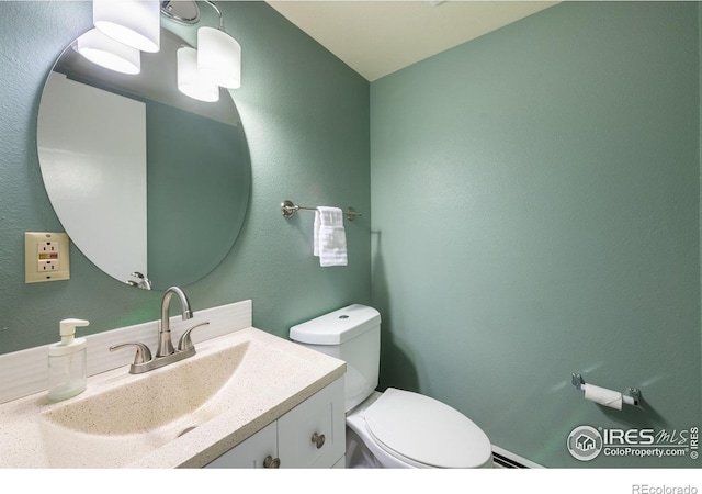 half bathroom featuring a textured wall, vanity, and toilet