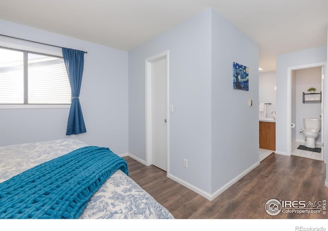 bedroom with connected bathroom, baseboards, and wood finished floors