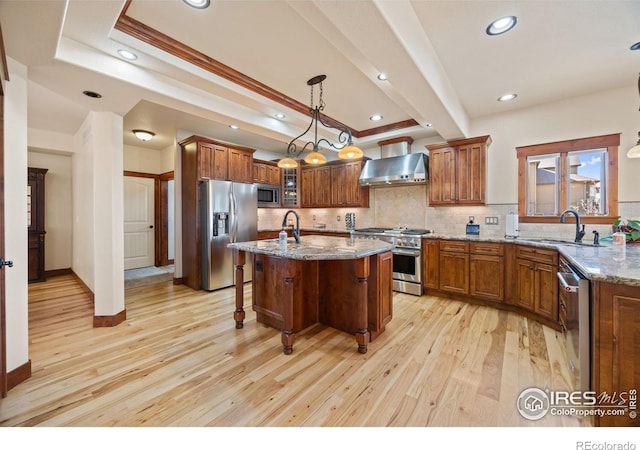 kitchen featuring wall chimney exhaust hood, appliances with stainless steel finishes, brown cabinets, and a sink