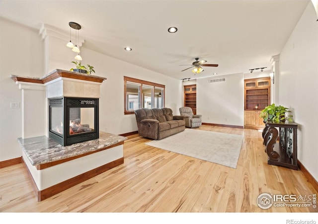 living room featuring a ceiling fan, light wood-type flooring, a fireplace, and baseboards