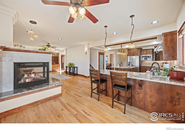 kitchen featuring brown cabinets, a fireplace, decorative light fixtures, appliances with stainless steel finishes, and light wood-style floors