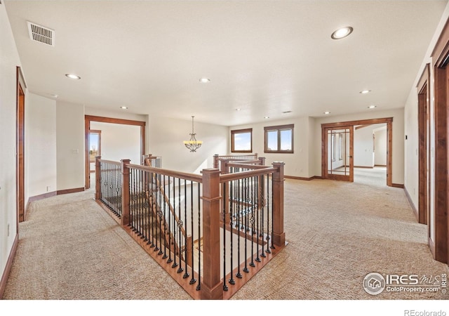 hallway featuring baseboards, visible vents, light carpet, and an upstairs landing