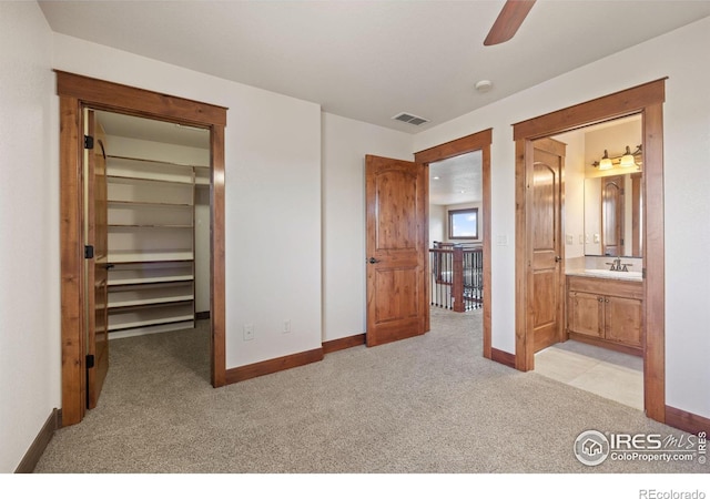 bedroom featuring a walk in closet, light colored carpet, a sink, and baseboards