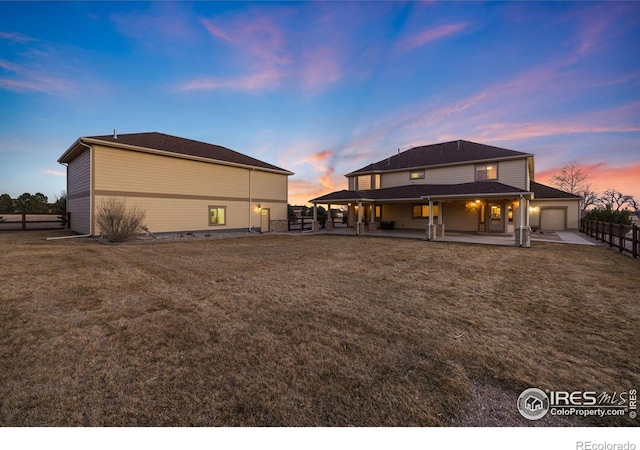 back of house at dusk featuring a yard, fence, an attached garage, and a patio