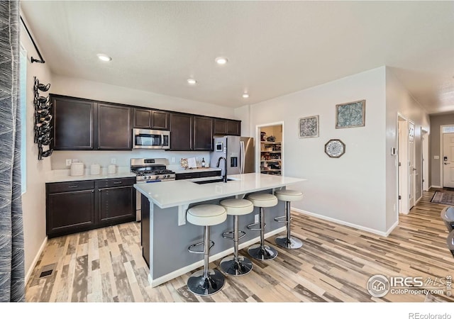 kitchen with a kitchen breakfast bar, light countertops, appliances with stainless steel finishes, light wood-type flooring, and a center island with sink