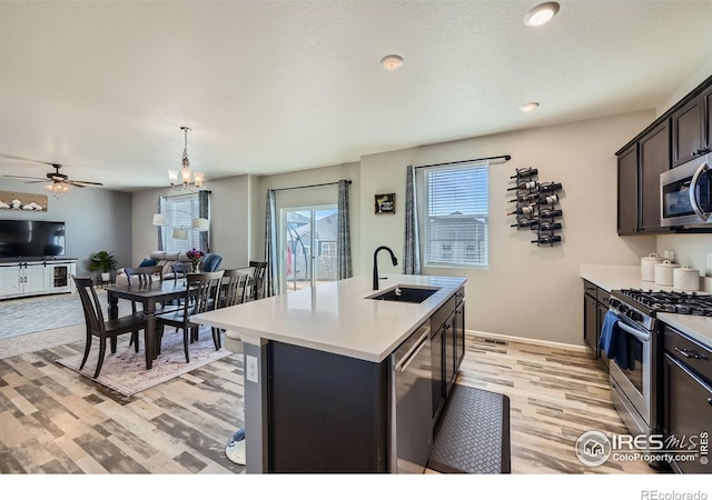 kitchen with open floor plan, stainless steel appliances, light countertops, light wood-style floors, and a sink