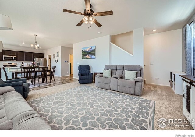 living area featuring baseboards, ceiling fan with notable chandelier, recessed lighting, and light colored carpet