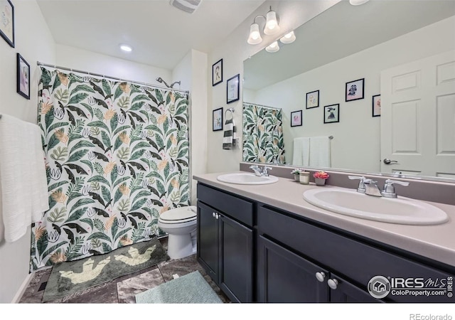 bathroom with visible vents, double vanity, a sink, and toilet