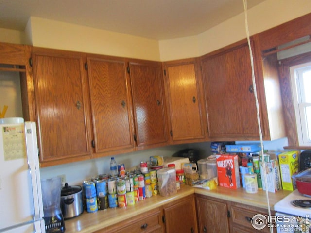 kitchen featuring light countertops, brown cabinetry, and freestanding refrigerator