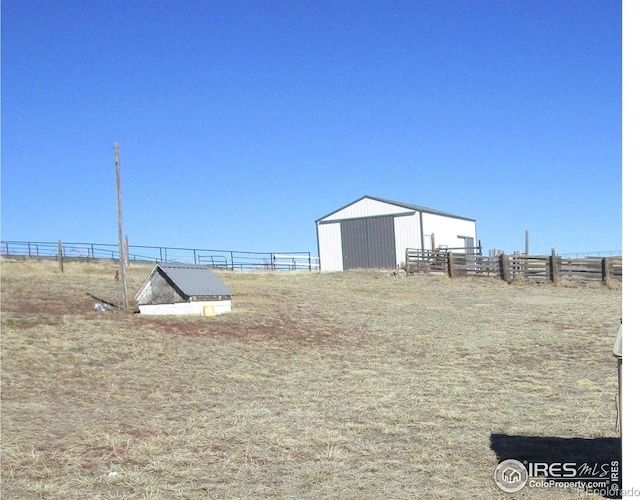 view of yard featuring a rural view, fence, a pole building, and an outbuilding