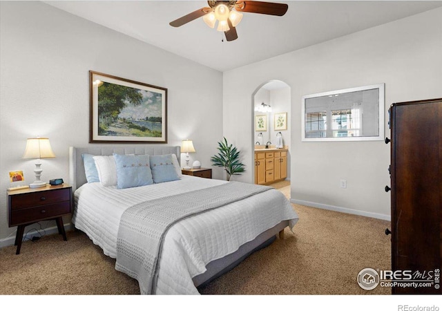 bedroom with arched walkways, light carpet, connected bathroom, and baseboards