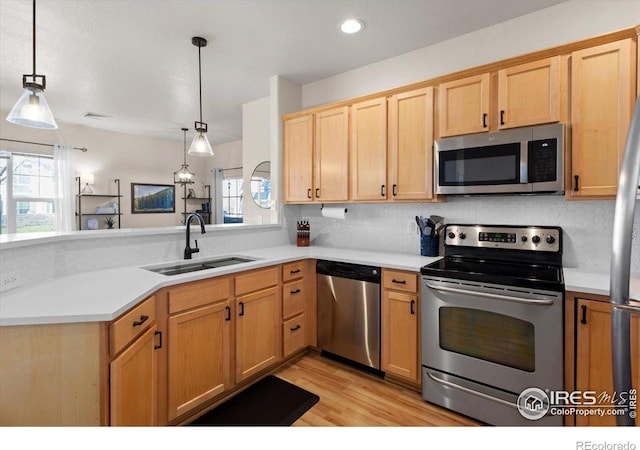 kitchen featuring appliances with stainless steel finishes, light countertops, a sink, and pendant lighting