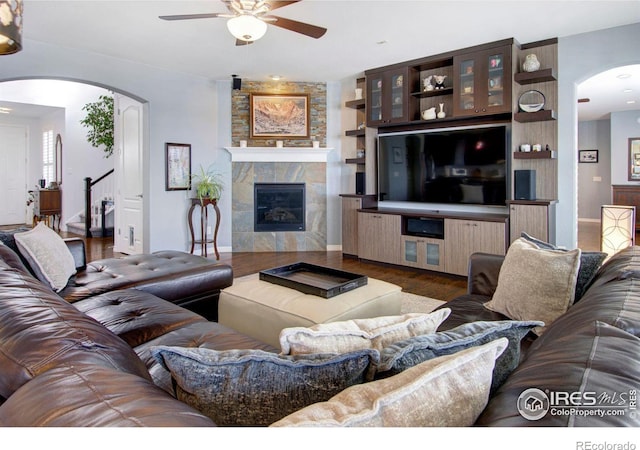 living area featuring arched walkways, stairway, a ceiling fan, wood finished floors, and a tile fireplace