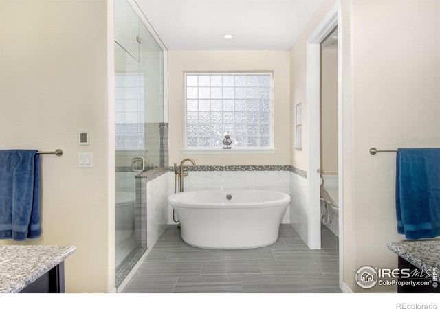 full bath featuring tile walls, a soaking tub, toilet, vanity, and a shower stall