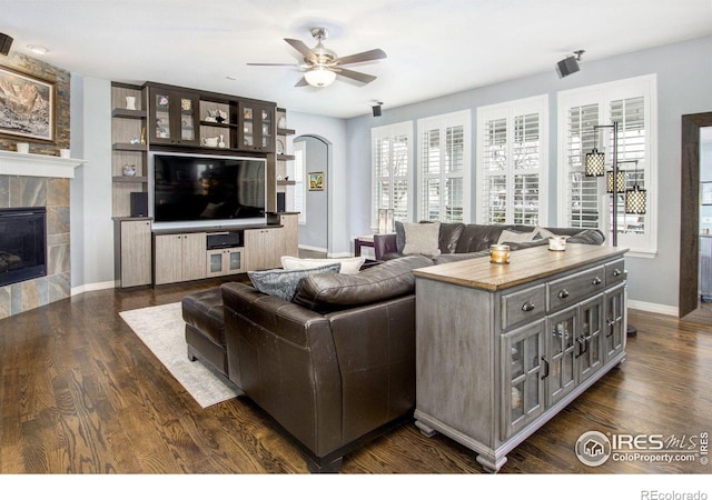 living area featuring baseboards, a fireplace, a ceiling fan, and dark wood-type flooring