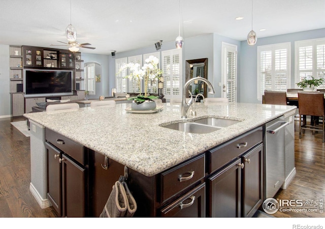 kitchen with dark wood-style floors, stainless steel dishwasher, a kitchen island with sink, dark brown cabinetry, and a sink