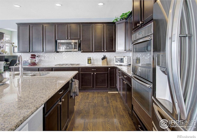 kitchen featuring decorative backsplash, dark wood-style flooring, stainless steel appliances, dark brown cabinets, and a sink