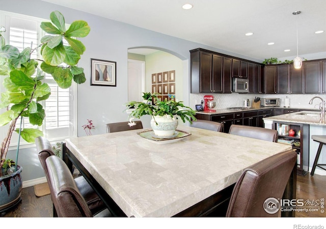 kitchen with dark wood-style floors, appliances with stainless steel finishes, dark brown cabinetry, a sink, and a kitchen island