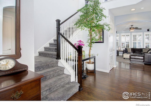 stairway with arched walkways, wood finished floors, a ceiling fan, and baseboards