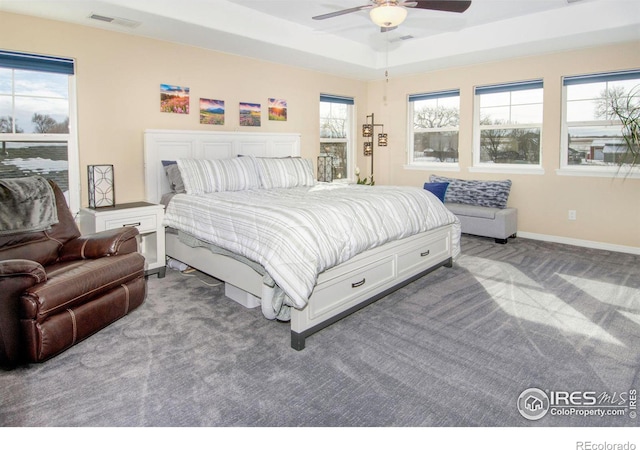 carpeted bedroom with ceiling fan, a tray ceiling, visible vents, and baseboards