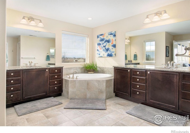 full bath featuring a garden tub, two vanities, and a sink