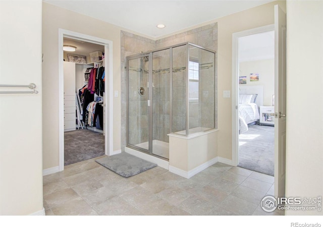 ensuite bathroom featuring a spacious closet, a stall shower, connected bathroom, and baseboards