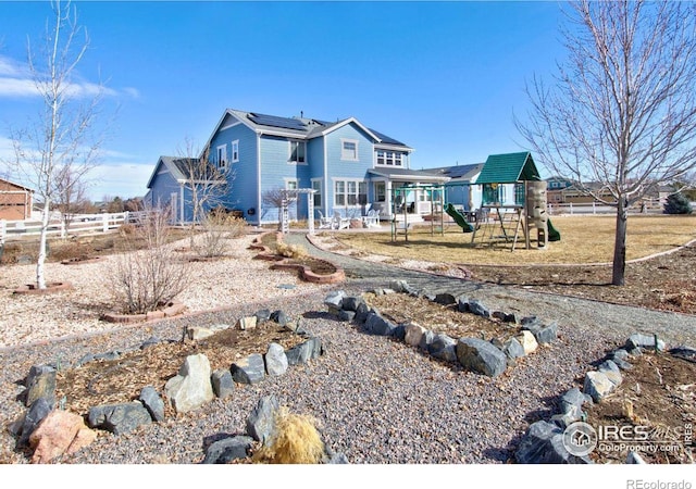 view of front of property featuring a playground, fence, and solar panels