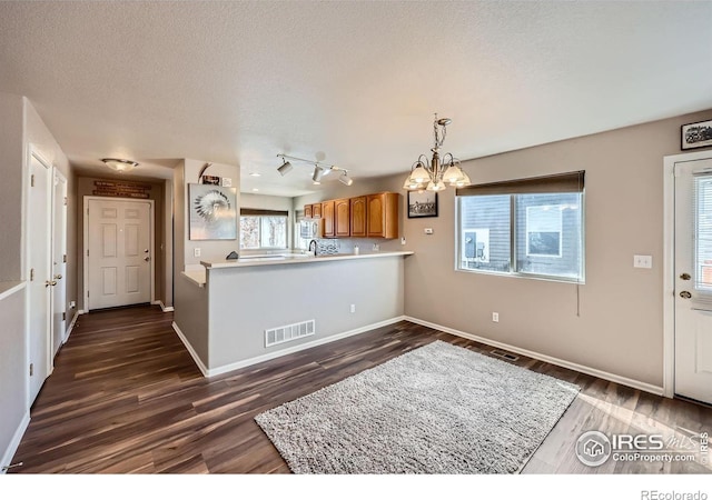 kitchen featuring visible vents, dark wood-type flooring, brown cabinetry, a textured ceiling, and a chandelier