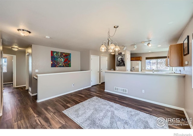 kitchen featuring visible vents, baseboards, freestanding refrigerator, brown cabinetry, and dark wood finished floors