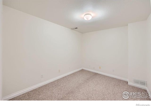 empty room with light colored carpet, visible vents, a textured ceiling, and baseboards