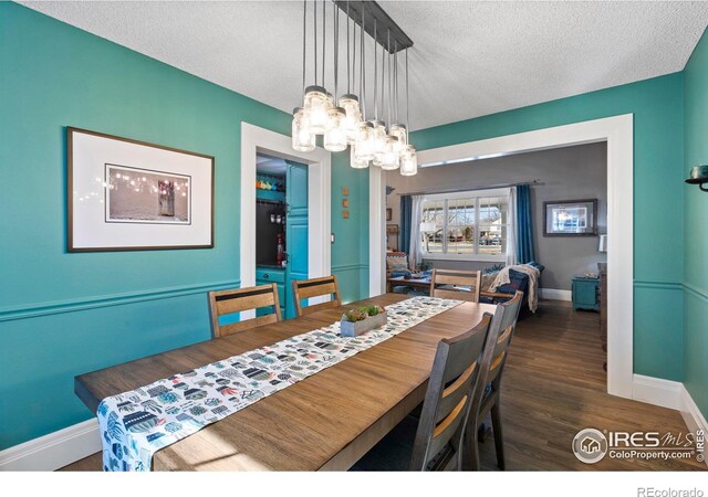 dining space featuring a textured ceiling, baseboards, a notable chandelier, and wood finished floors