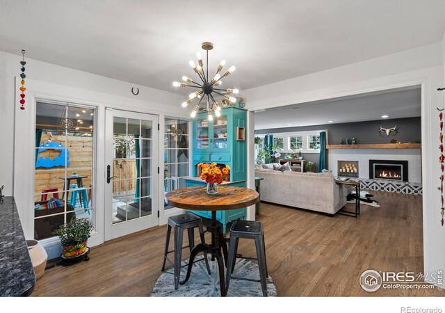 dining room with a warm lit fireplace, an inviting chandelier, and wood finished floors