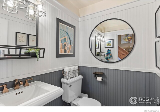 half bathroom featuring wainscoting, a sink, toilet, and an inviting chandelier