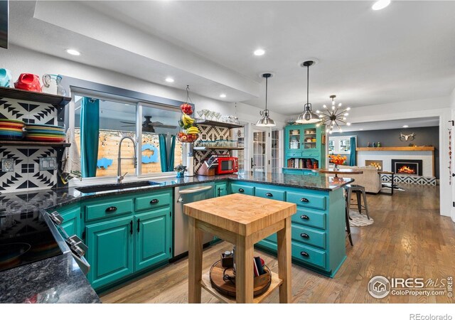 kitchen featuring a peninsula, wood finished floors, a sink, a lit fireplace, and stainless steel dishwasher