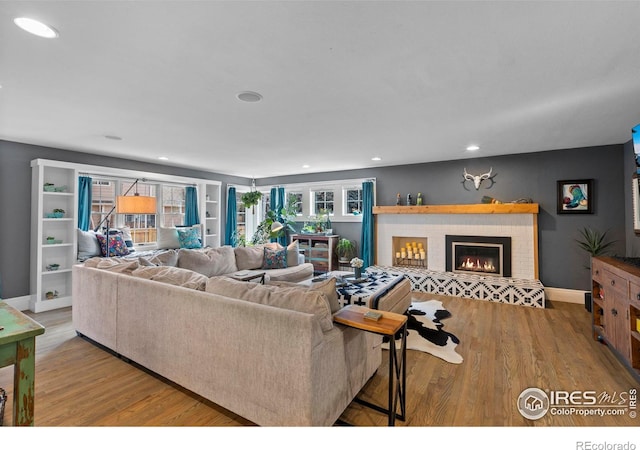 living area featuring recessed lighting, a fireplace, wood finished floors, and baseboards