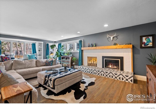 living area featuring a brick fireplace, baseboards, a wealth of natural light, and wood finished floors