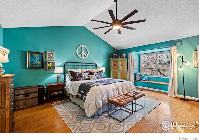 bedroom featuring a ceiling fan, vaulted ceiling, a textured ceiling, wood finished floors, and baseboards