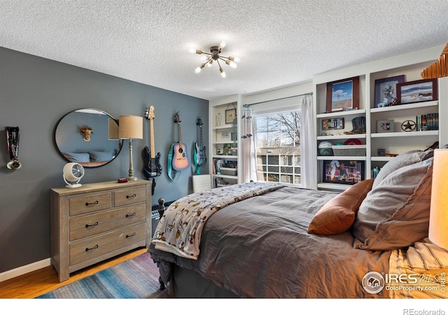 bedroom with a textured ceiling, wood finished floors, and baseboards