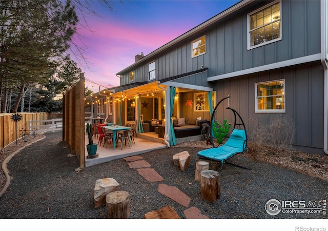 back of house with a patio, a chimney, an outdoor hangout area, board and batten siding, and fence