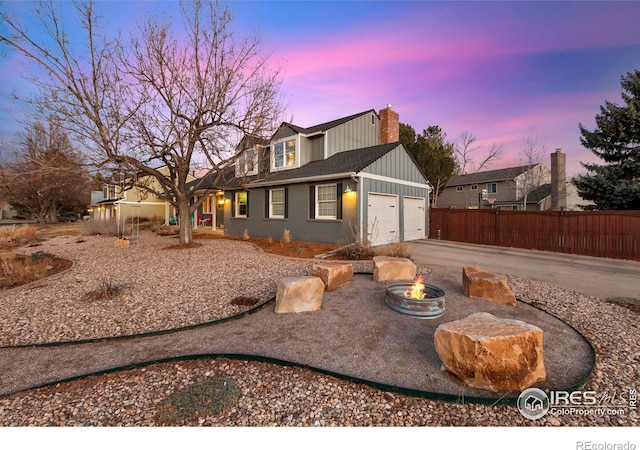 view of front of home with an outdoor fire pit, concrete driveway, a chimney, an attached garage, and fence