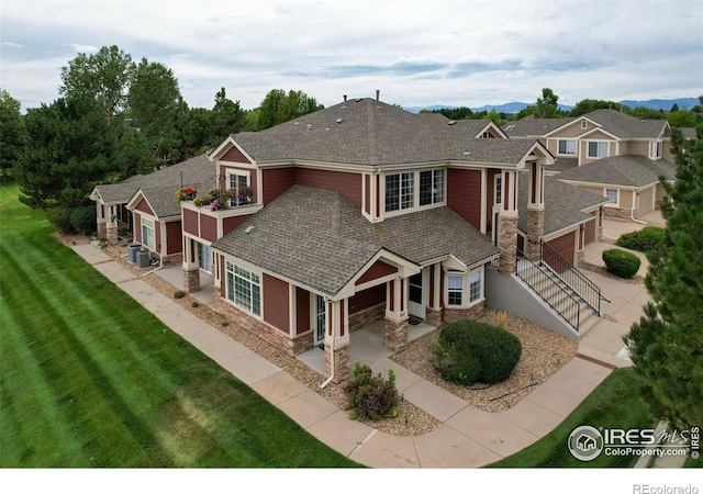 view of front of home with central AC unit, a shingled roof, concrete driveway, stone siding, and a front lawn