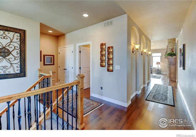 hall featuring baseboards, visible vents, hardwood / wood-style flooring, an upstairs landing, and recessed lighting