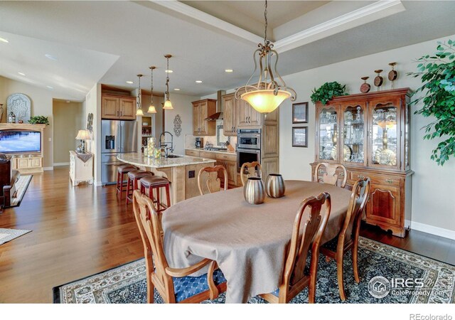 dining space featuring baseboards, a raised ceiling, wood finished floors, and recessed lighting