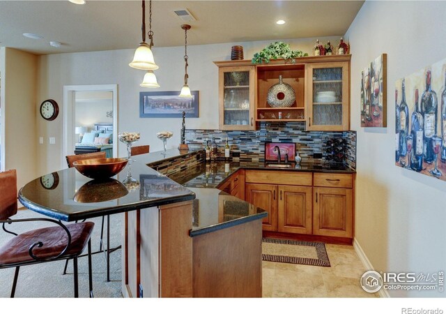 kitchen featuring visible vents, brown cabinets, tasteful backsplash, a kitchen bar, and glass insert cabinets