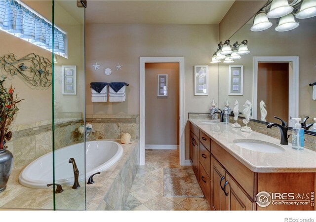 full bathroom featuring a relaxing tiled tub, a sink, baseboards, and double vanity