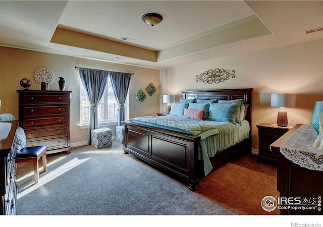 carpeted bedroom featuring a tray ceiling, visible vents, and baseboards