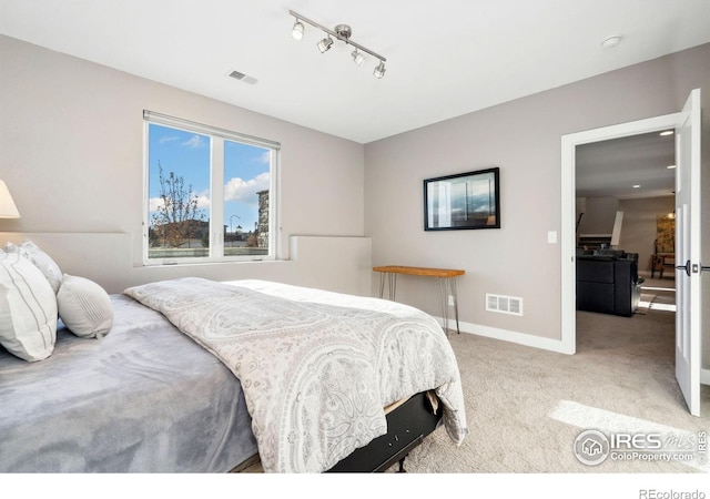 carpeted bedroom featuring rail lighting, visible vents, and baseboards