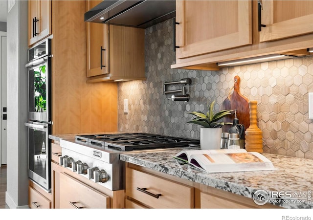 kitchen with stainless steel appliances, ventilation hood, backsplash, and light stone countertops