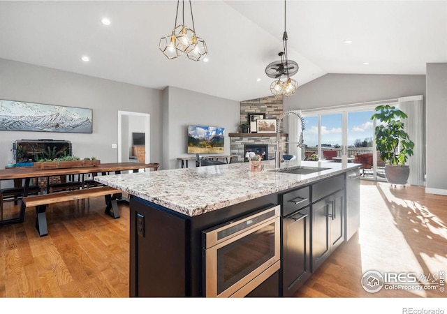 kitchen featuring open floor plan, stainless steel microwave, a sink, and a stone fireplace