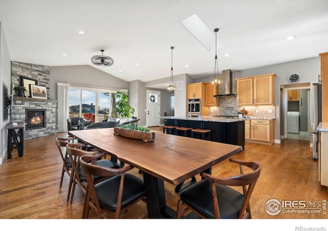 dining area featuring a fireplace, light wood finished floors, lofted ceiling, recessed lighting, and washer / dryer